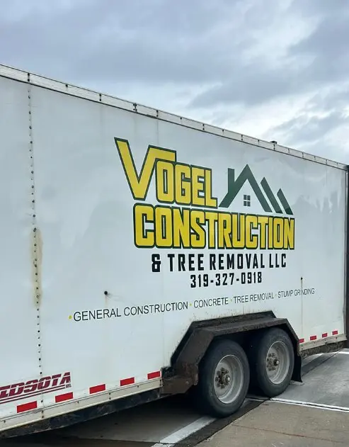 Vogel Construction & Tree Removal LLC branded white trailer parked on pavement showing large yellow and green company logo, phone number, and services listed—general construction, concrete, tree removal, stump grinding.